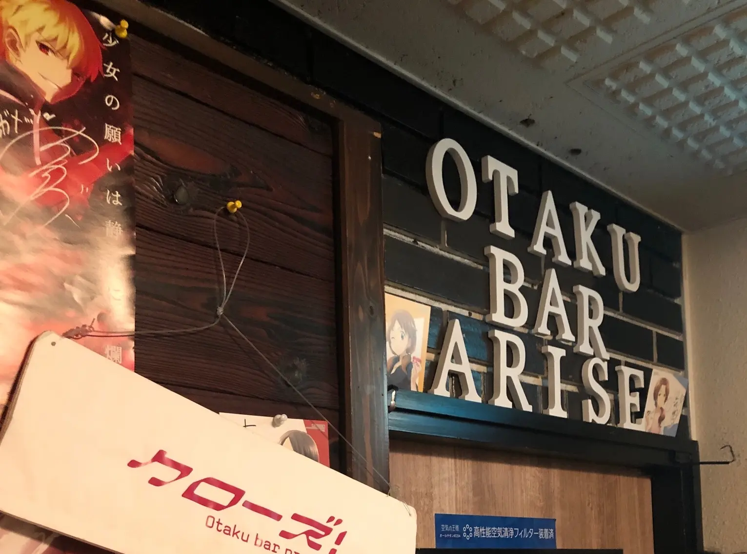 扉の上に「OTAKU BAR ARAISE」と書かれていて、扉の横の壁には「クローズ!」と書かれた看板がかかっている