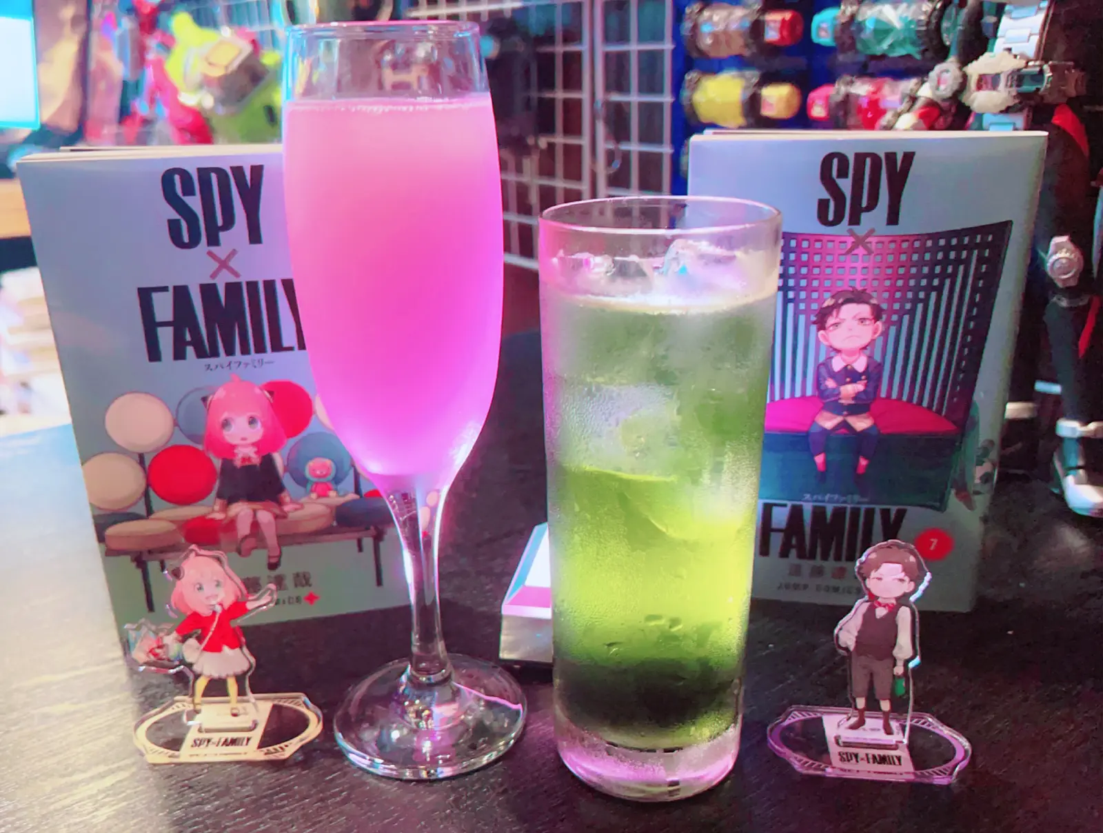 ピンク色のカクテルと緑色のカクテルの脇に「SPY×FAMILY」のアーニャとダミアンのアクリルスタンドが立てられている