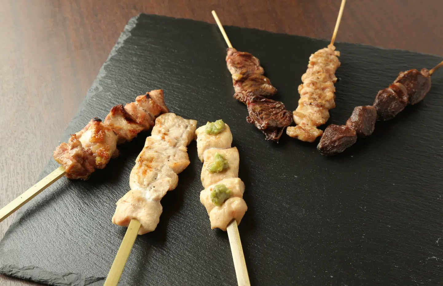 木目のある黒いお皿に6種類の焼き鳥が1種類ずつ並べられている