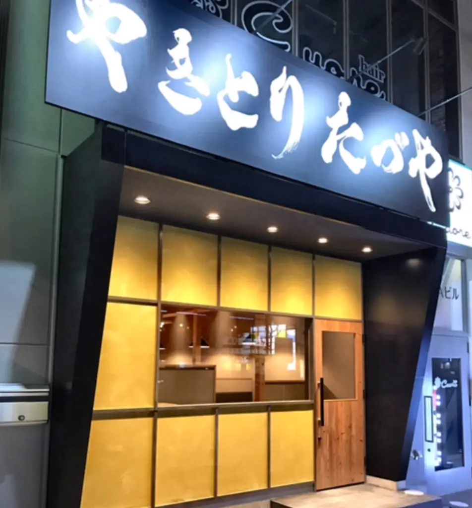 照明のついた明るい外装に大きな窓があり、その上には黒ベースで白字の「やきとり たづや」と書かれた看板がある